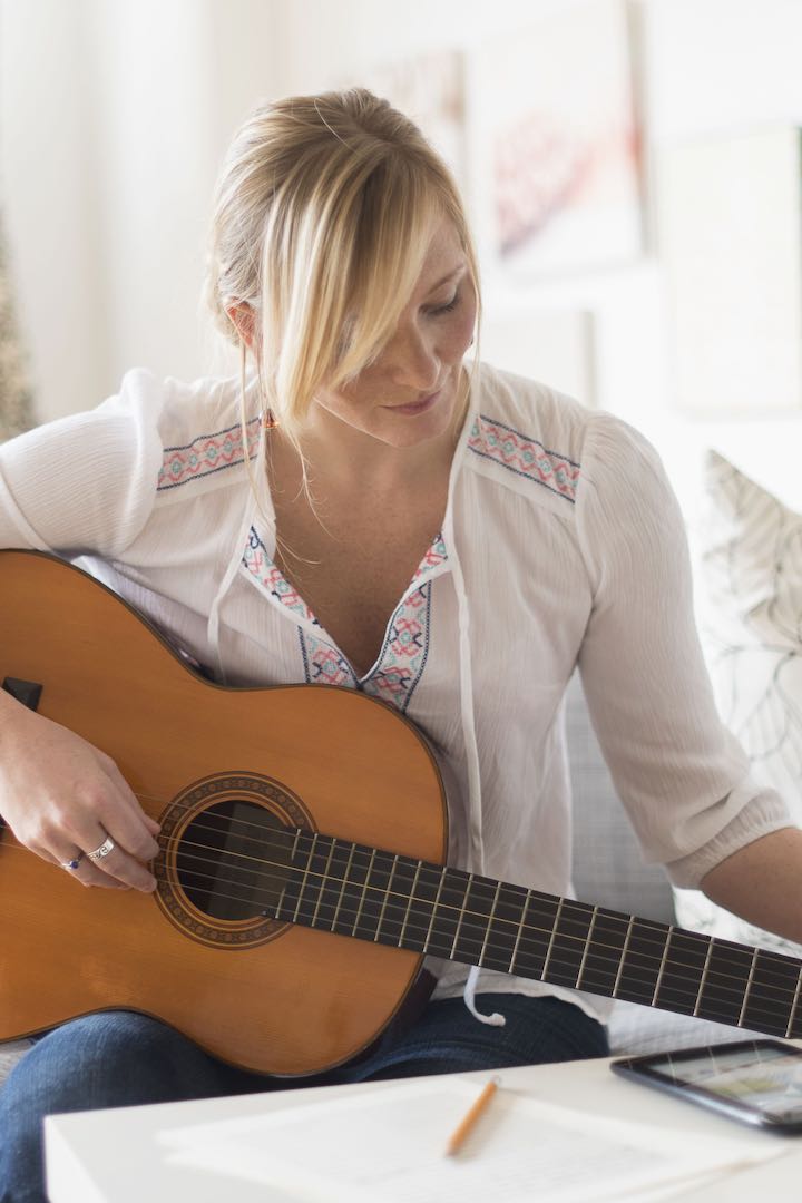 woman on couch writing song with guitar